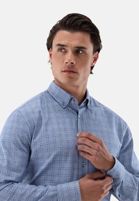 Himmelblaues Hemd mit Knopfleiste, das ein kariertes Muster aus blauen und weißen Quadraten aufweist und aus einem weichen Stoff gefertigt ist. Verstellbare Manschetten mit Knöpfen.