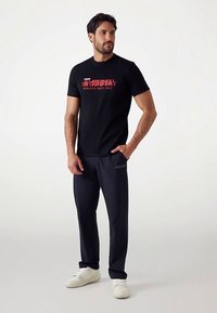 Svart t-shirt med kort ärm och röd grafisk text, kombinerad med marinblå byxor och vita sneakers. Avslappnad sportig design med lös passform.