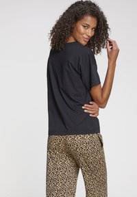 Schwarzes, lässig geschnittenes Baumwoll-T-Shirt mit kurzen Ärmeln, kombiniert mit beigen Hosen im Leopardenmuster.