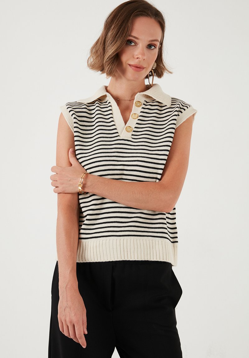 Mouwloze gestreepte gebreide sweater met een v-hals en ribgebreide zoom. Kleuren zijn zwart en crème, met drie gouden knopen op de kraag.