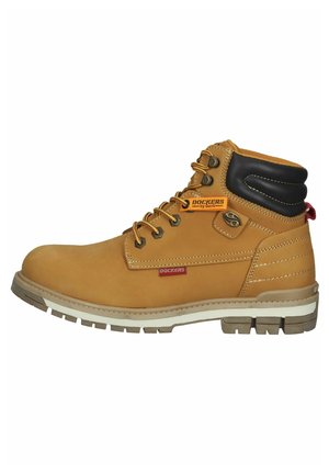 Botas de tobillo de cuero marrón con un cuello acolchado negro, cordones amarillos y una suela blanca y gris. Presenta una etiqueta de marca en el costado.