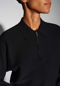 Pull-over en maille noire avec fermeture éclair à l'avant et col pointu. Tissu texturé et coupe ajustée mettant en valeur le col.