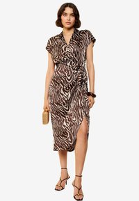 Bruin en crèmekleurig zebra-print jurk met een wikkelontwerp, korte mouwen, een zijsplit en een lichte stof. In combinatie met zwarte sandaaltjes met bandjes.