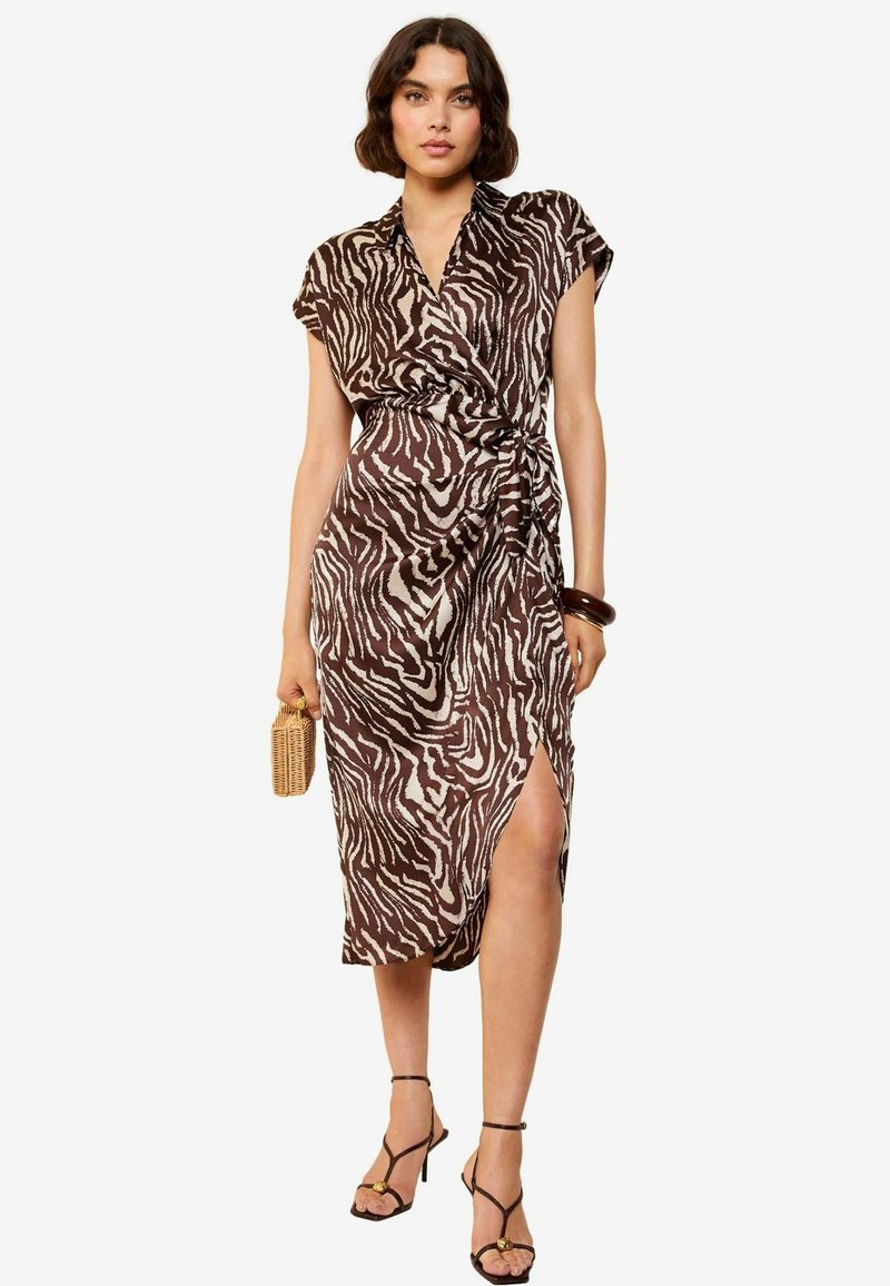 Bruin en crèmekleurig zebra-print jurk met een wikkelontwerp, korte mouwen, een zijsplit en een lichte stof. In combinatie met zwarte sandaaltjes met bandjes.