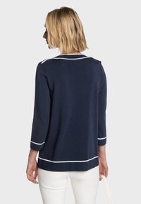 Pull bleu marine à manches trois-quarts, bordure blanche autour du col et de l'ourlet, en tissu tricoté texturé.