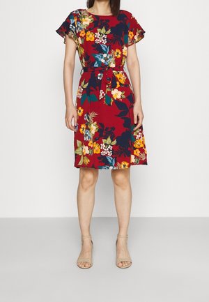 Robe fleurie longueur genou en rouge, avec des manches courtes volantées, une taille cintrée avec un lien, et des motifs floraux vibrants en jaune, bleu et vert.