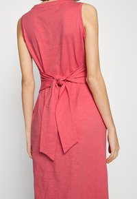 Ärmlös rosa klänning med knytning i midjan, mjuk textur och avslappnad passform, med en enkel rund halsringning och inga synliga mönster.