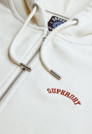 Hvid hættetrøje med lynlås i sølv, snore med metalender og rød broderet "SUPERDRY"-logo på brystet.