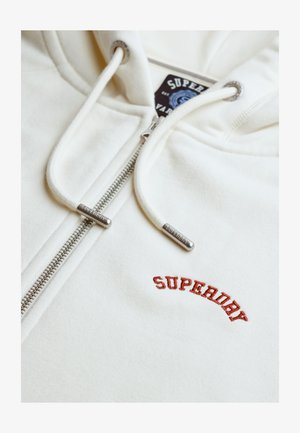 Hvid hættetrøje med lynlås i sølv, snore med metalender og rød broderet "SUPERDRY"-logo på brystet.