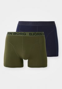 Dve páry pánskych boxeriek v olivovo zelenej a námorníckej modrej farbe. Vyrobené z mäkkej tkaniny s tesným strihom. Každé má elastický opasok s logom.