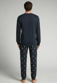 Námořnický modrý dlouhý rukáv a tmavé pyžamové kalhoty s malými červenými a zelenými vzory, měkká látka a žebrované manžety. Pohodlná souprava na domácí nošení.