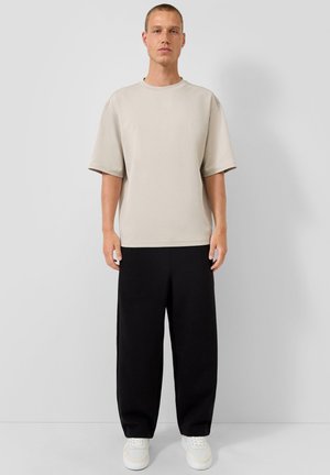 Camiseta beige de gran tamaño con mangas cortas, combinada con pantalones negros holgados y zapatillas blancas, diseño minimalista, textura suave.