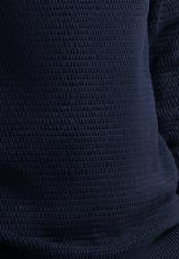 Close-up van een donkerblauwe gebreide trui stof met een gedetailleerd geweven patroon en stiksels.