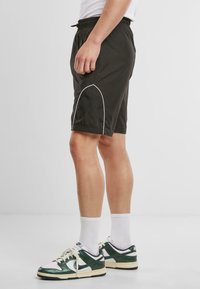 Shorts de sport noirs avec une taille élastique et des détails de couture blanche, associés à des baskets vertes et blanches et des chaussettes blanches mi-mollet.