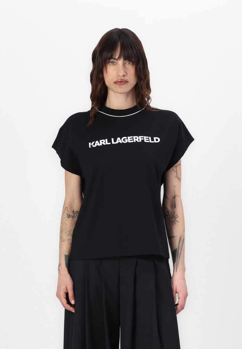 Melnā, īsa piedurkņu T-kreklā ar apaļu kakla izgriezumu, uz kura priekšpuses ir uzdrukāts uzbolds balts teksts "KARL LAGERFELD". Mīksts audums, brīvs griezums.
