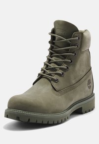 Bottine en cuir vert olive à lacets avec col rembourré, semelle robuste et logo Timberland embossé sur le côté.
