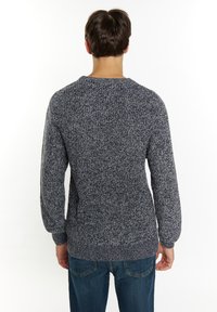 Tamsiai mėlynas megztinis su tekstūruotu paviršiumi, ilgomis rankovėmis ir apvalia iškirpte. Užmautas su mėlynomis džinsomis, matomas iš nugaros.