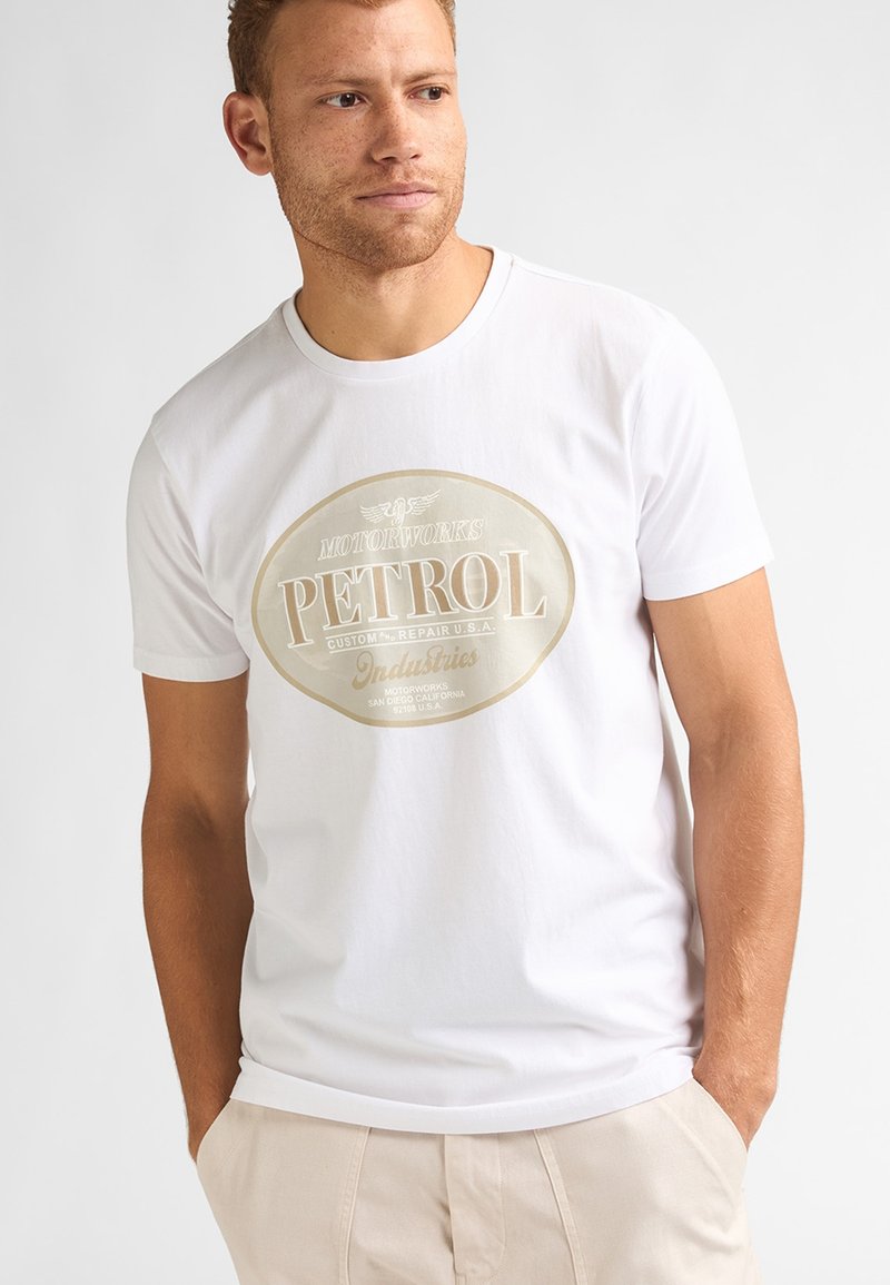 T-shirt en coton blanc arborant un grand graphisme ovale doré et noir avec l'inscription « PETROL », au design vintage et à la texture douce.