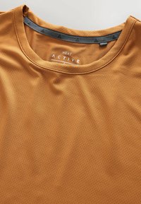 Koszulka sportowa w ciepłym odcieniu pomarańczowym, wykonana z teksturowanej siateczkowej tkaniny, z okrągłym dekoltem i metką z napisem "NEXT ACTIVE".