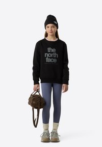 Μαύρο φούτερ με λογότυπο "the north face", μπλε κολάν, μπεζ πλεκτές κάλτσες, γκρι αθλητικά παπούτσια και καφέ τσάντα με υφή. Μαύρο σκουφάκι στο κεφάλι.