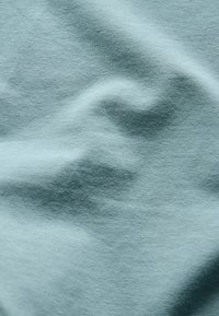 Tissu en coton bleu clair avec une texture lisse, affichant des plis et des rides doux, créant des variations subtiles de couleur et d'ombrage.