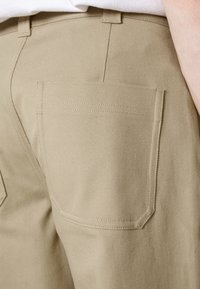 Beige kalhoty vyrobené z texturované látky, s zadní kapsou s čistým švem a přímým střihem. Viditelný pas a poutka na pás.