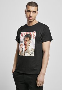 Black cotton t-shirt featuring a graphic print of a character from "Scarface," with bold red text and a distressed design.