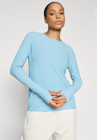 Tricou sport cu mânecă lungă, de culoare albastră deschisă, realizat dintr-un material texturat, cu orificii pentru degete, având un decolteu rotund și o marcă minimală.