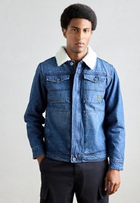 Jeansjacke mit einem weichen, weißen Kunstfellkragen. Verfügt über zwei Brusttaschen und einen Reißverschluss. Klassische blaue Waschung und lockere Passform.