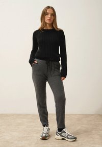 Svart ribbat stickat tröja med långa ärmar, parat med gråa byxor med dragsko. Modellen bär grå och vita sportskor.