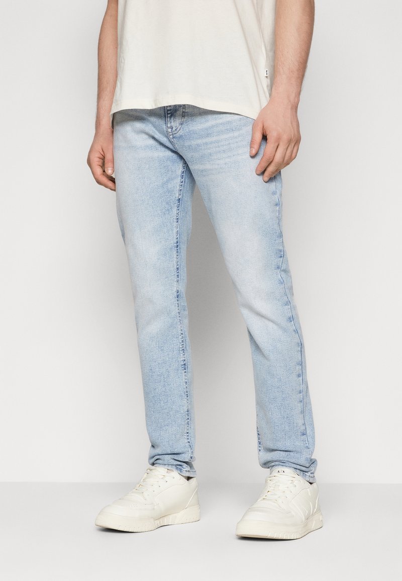 Ljusblå denimjeans med rak passform, med subtila slitningar och en standard femfickdesign, kombinerat med vita sneakers.