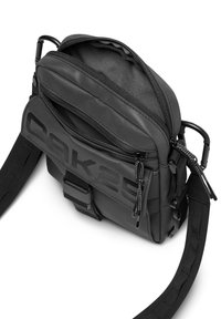 Svart nylon axelväska med flera zip-fack, justerbar rem och präglad logotyp. Kompakt rektangulär design.