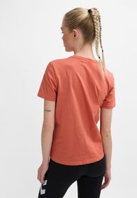 Kortærmet T-shirt i koralfarvet bomuld med rund halsudskæring og afslappet pasform, parret med sorte leggings med hvidt logo-detalje.