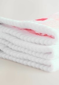 Gomila mekih bijelih ručnika s teksturiranom tkaninom; jedan ručnik ima ružičasti uzorak. Rubovi su uredno poravnati.