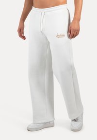 Weiße Sweatpants mit lässiger Passform, elastischem Bund, Kordelzug, Seitentaschen und dezenter "Smilodons"-Schrift in Beige auf der Vorderseite.