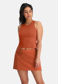 Oranje sportieve crop top met een ronde halslijn en een bijpassende rok. Beide zijn gemaakt van een gladde, elastische stof met een slim fit design en zijzakken.