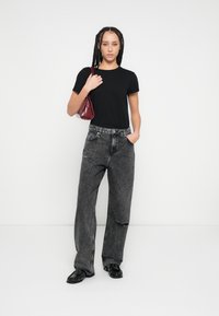 Fekete pamut póló, laza szabású szürke farmernadrág kopott részlettel, fényes fekete cipővel és egy kis bordó kézitáskával párosítva.