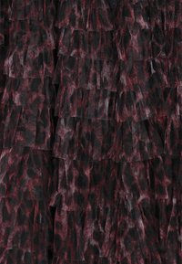 Tesătură cu un print leopard în nuanțe roșii și negre, stratificată, având o textură din plasă transparentă, aranjată în volane orizontale.