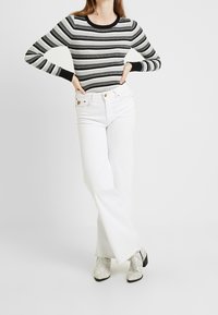 Pasek czarno-szary top z długim rękawem zestawiony z białymi dzwonowatymi jeansami. Stylizację dopełniają białe botki z motywem skóry węża.