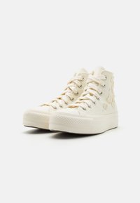 Wysokie trampki w kolorze off-white z płótna, z metalowymi oczkami i teksturowanymi gumowymi podeszwami. Kwiatowe hafty po bokach.