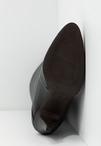 Černá kožená kotníková bota s kulatou špičkou, hladkým povrchem a gumovou podrážkou s rýhovanými detaily. Velikost označena jako 37.