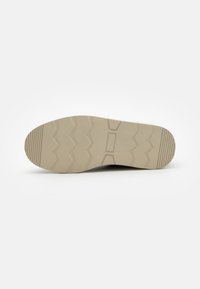 Suela de zapato en goma beige con un patrón de banda de rodadura en zigzag, centro liso y borde ligeramente redondeado para tracción y estabilidad.