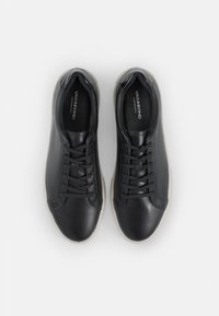 Pereche de adidași negri din piele, cu șireturi negre și tălpi de culoare deschisă, văzuți de sus pe un fundal alb.