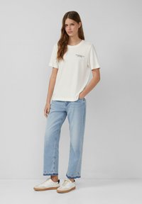 Witte katoenen T-shirt met korte mouwen en een ronde halslijn, voorzien van marineblauwe tekst. Gekoeld met lichtblauwe denim jeans en witte sneakers.
