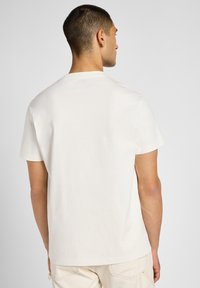 T-shirt bianco in cotone con maniche corte, scollo rotondo e vestibilità standard. Il tessuto appare morbido e leggermente testurizzato. Nessun motivo visibile.