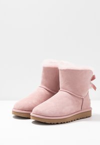 Bottines en daim rose avec une doublure douce en fourrure, dotées d'un bout arrondi, d'un détail ruban à l'arrière et d'une semelle en caoutchouc texturée.