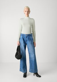 Gaiši zaļa pieguļoša turtlenecks, augstās jostas blue platās bikses ar apkaklēm, melni potīšu zābaki un melna austo soma.