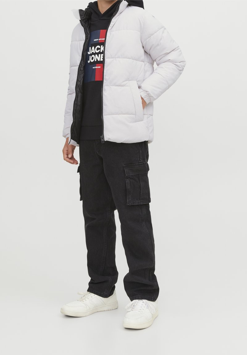 Jasnoszara kurtka puchowa na zamek, czarna bluza z kapturem z logo, czarne spodnie cargo oraz białe sneakersy. Nacisk na funkcjonalność i wygodę.