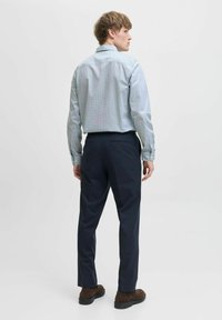 Camicia a quadri azzurri chiari con bottoni abbinata a pantaloni blu scuro. La camicia presenta una consistenza morbida e una vestibilità strutturata. Scarpe marroni completano il look.