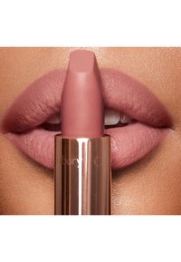 Mattweite rosa Lippenfarbe mit rechteckigem Lippenstiftkopf, vor sanften, volleren rosa Lippen gehalten. Die Lippenstiftverpackung hat ein glänzendes roségoldenes Finish.